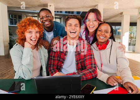 Smiling multiracial group of young students looking at camera, sitting together in university library with a laptop, books, and notebooks. Diverse classmates studying and collaborating at university. High quality photo Stock Photo