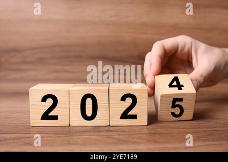 2025 New Year. Woman turning wooden cube on table, closeup Stock Photo