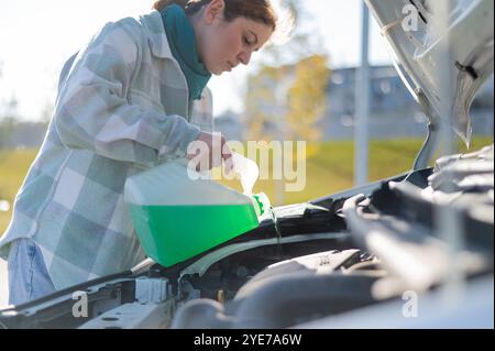 Caucasian woman filling car reservoir with windshield washer fluid from bottle.  Stock Photo