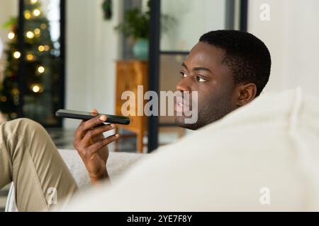 African American man using smartphone voice command at home during Christmas Stock Photo