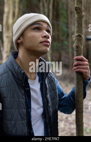 Young man in winter clothing exploring forest, holding tree branch thoughtfully Stock Photo