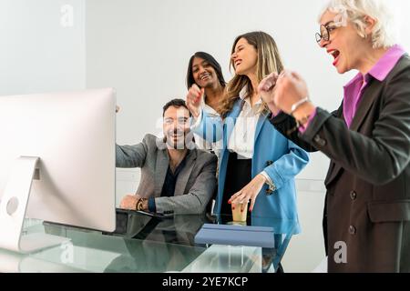 Excited diverse business professionals celebrating success while looking at computer monitor in modern office. Young and senior employees sharing joyf Stock Photo