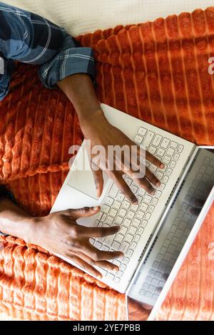 Typing on laptop, African american man working from home on cozy orange blanket Stock Photo