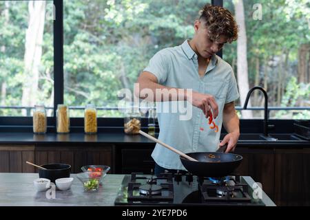 Young man cooking in modern kitchen, adding red peppers to stir-fry, at home Stock Photo