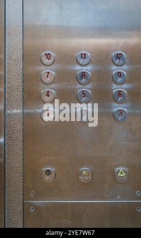 Round metallic buttons on a 12 storey elevator control panel with signs of wear. Stock Photo