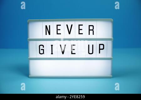 Never Give Up letterboard text on LED Lightbox on blue background Stock Photo