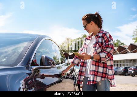 Urban woman unlocking parked car remotely using her smartphone. Car-sharing service. Automotive wireless technologies. Stock Photo