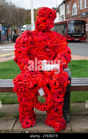 Chesham, Buckinghamshire, UK. 29th October, 2024. A striking Remembrance Day figure of man covered in red poppies sitting on a seat in Chesham next to the war memorial and holding a white dove. Credit: Maureen McLean/Alamy Live News Stock Photo