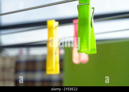 Green, yellow and pink plastic clothespins hanging on an outdoor clothes dryer: close-up. Using clothespins to hold washed clothes when drying outside Stock Photo