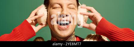 This cheerful young man smiles broadly while covering his ears with soft earmuffs. Stock Photo