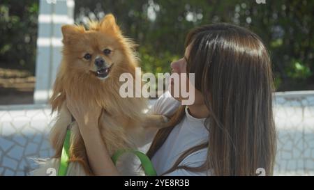 A young woman lovingly gazes at her pomeranian dog while sitting in an urban park. Stock Photo