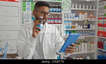 Young african american male pharmacist examining medication while holding a tablet in a drugstore Stock Photo