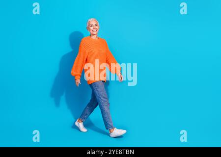Photo of elderly woman going wearing autumn season outfit isolated blue color background Stock Photo