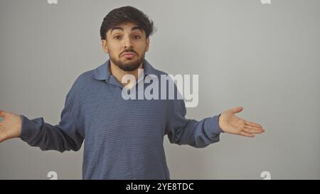 Confused young man with a beard standing against a white background, expressing uncertainty with outstretched hands. Stock Photo