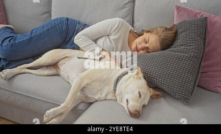 A young woman peacefully napping on a couch next to her resting dog in a cozy living room. Stock Photo