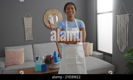 Woman smiling indoors in modern living room, wearing apron and gloves, with cleaning supplies on table, representing young, latin, beautiful, female, Stock Photo