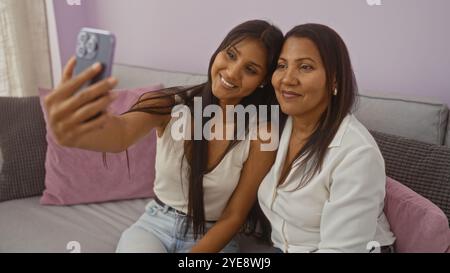 Mother and daughter taking a selfie together in the living room of their home, showing family love and connection between two women Stock Photo