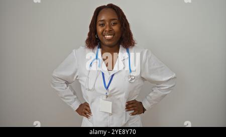 Female african american doctor stands confidently with stethoscope over white background smiling in medical uniform Stock Photo