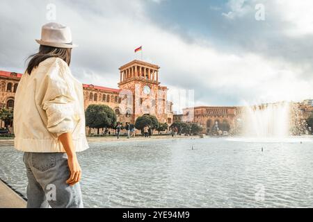 Close up woman tourist wear white jacket visit famous destination Armenia capital Yerevan. Clock bell tower with Armenian flag. Travel caucasus region Stock Photo