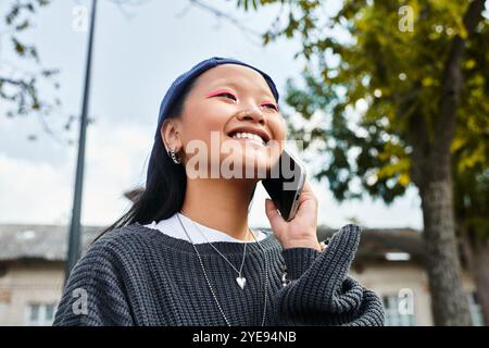 A cheerful young student girl smiles while talking on her phone, embracing vibrant youth culture outdoors. Stock Photo