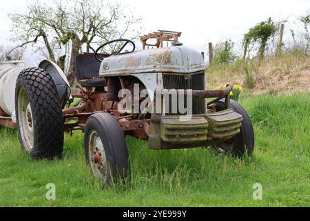 a rusty old tractor sitting idly in a field on a cloudy spring day. Stock Photo