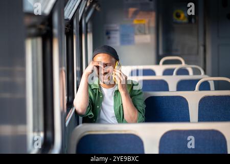 Cheerful man traveling by electric train, smiling talks on phone enjoying journey with positive mood Stock Photo