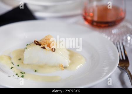 Dish of delicious cod fillet with a sauce and some garlic and pepper on top of it with rose wine at background. Stock Photo