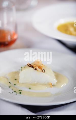 Dish of delicious cod fillet with a sauce and some garlic and pepper on top of it with rose wine at background. Stock Photo