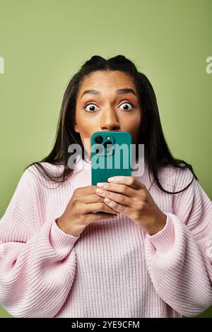 A young woman in warm, stylish clothes shows excitement while using her smartphone. Stock Photo
