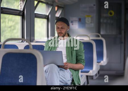 Focused thoughtful man passenger working on laptop while travel by electric train using earphones  Stock Photo