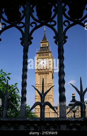 Low angle view of Big Ben (Elizabeth Tower) against a bright blue sky, the view framed by a decorative metal fence, London; London, England Stock Photo