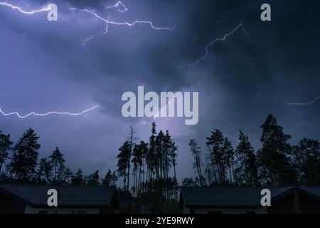 Dramatic night sky with bright lightning during a thunderstorm. Thunderstorm in the suburbs, forest and houses. Stock Photo