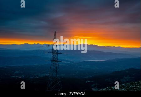 A dramatic mountain top view of the first ray of sunlight on a day with thick clouds, and a electricity tower in the foreground. Stock Photo