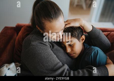Mother embracing son while sitting on sofa at home Stock Photo