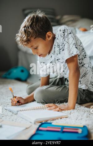 Focused boy doing homework while sitting on carpet at home Stock Photo