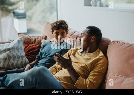 Father talking with son while sitting on sofa in living room at home Stock Photo