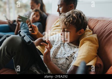 Curly haired boy using tablet PC while sitting with father on sofa at home Stock Photo
