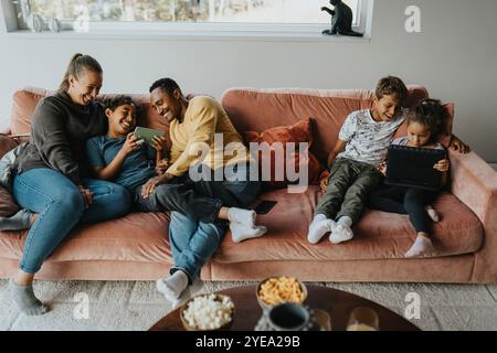 High angle view of multiracial happy family using wireless technologies while sitting on sofa at home Stock Photo