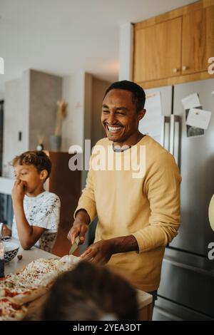Happy mature man making pizza with family while standing in kitchen at home Stock Photo