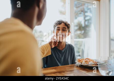 Father touching cheek of son sitting for lunch at dining table Stock Photo