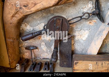 A vintage wheel brace hand drill, a bradawl, and hammer heads on a shelf. Stock Photo
