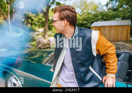 Happy man in letterman jacket leaning on vintage car Stock Photo