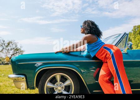 Side view of young woman leaning on vintage car in park under cloudy sky Stock Photo