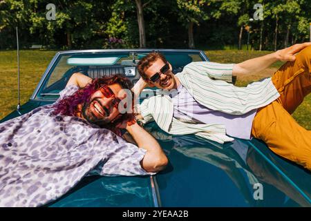Portrait of happy multiracial male friends lying on vintage car in park at sunny day Stock Photo