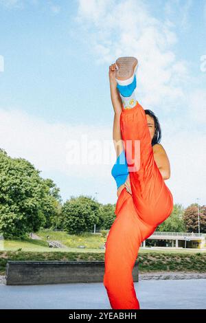 Athletic young woman kicking in air while standing near overpass under bridge Stock Photo