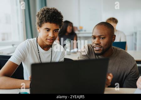 Male student and teacher using laptop at desk in classroom Stock Photo