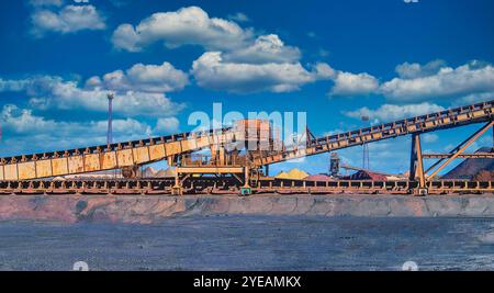 Loading iron ore conveyor machine on blue sky background in steel industry, UK Stock Photo