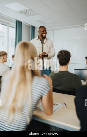 Happy male teacher gesturing while discussing with high school students in classroom Stock Photo