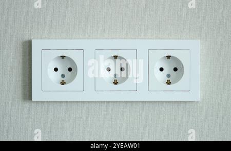 Electrical sockets in a triple plastic frame against the background of light wallpaper on the wall Stock Photo