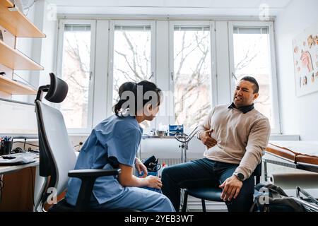 Man with stomachache discussing problems with female doctor while sitting in medical examination room Stock Photo